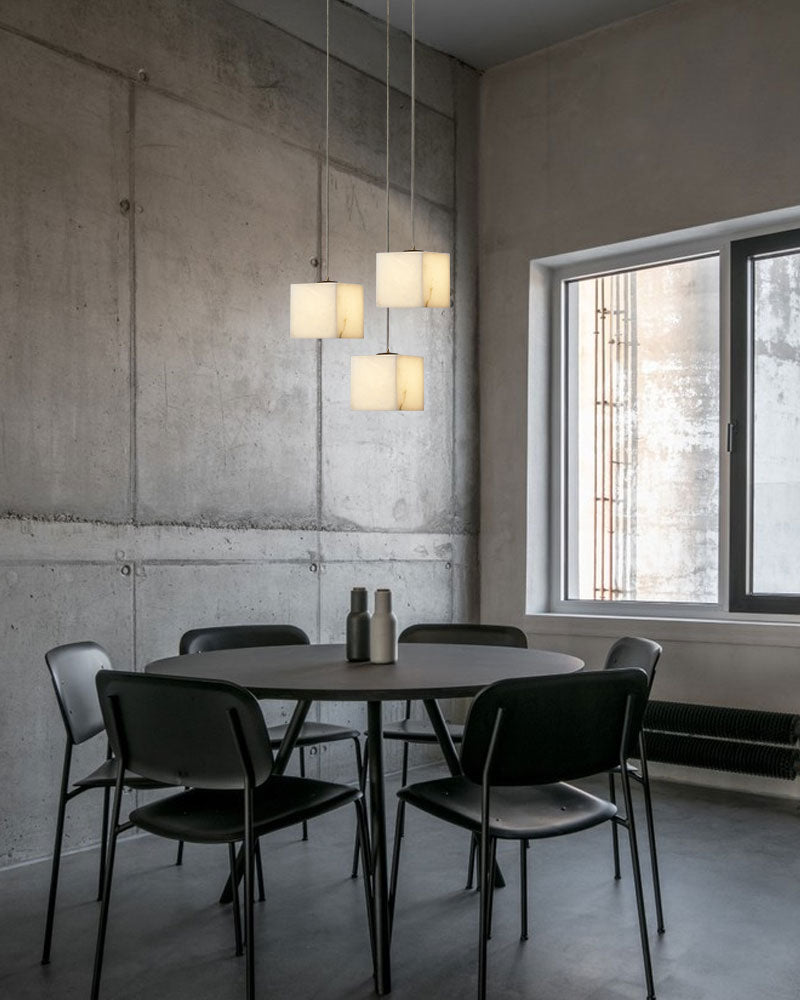 Square white alabaster chandelier over modern round dining table with black chairs.