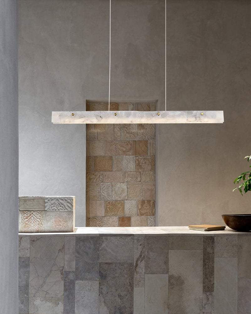 Long marble pendant light illuminating a minimalist kitchen countertop with neutral decor