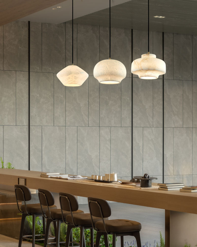 Three alabaster pendant lamps above a sleek bar with modern stools.