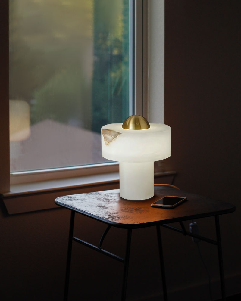 Modern alabaster table lamp with brass accent on a side table near a window.