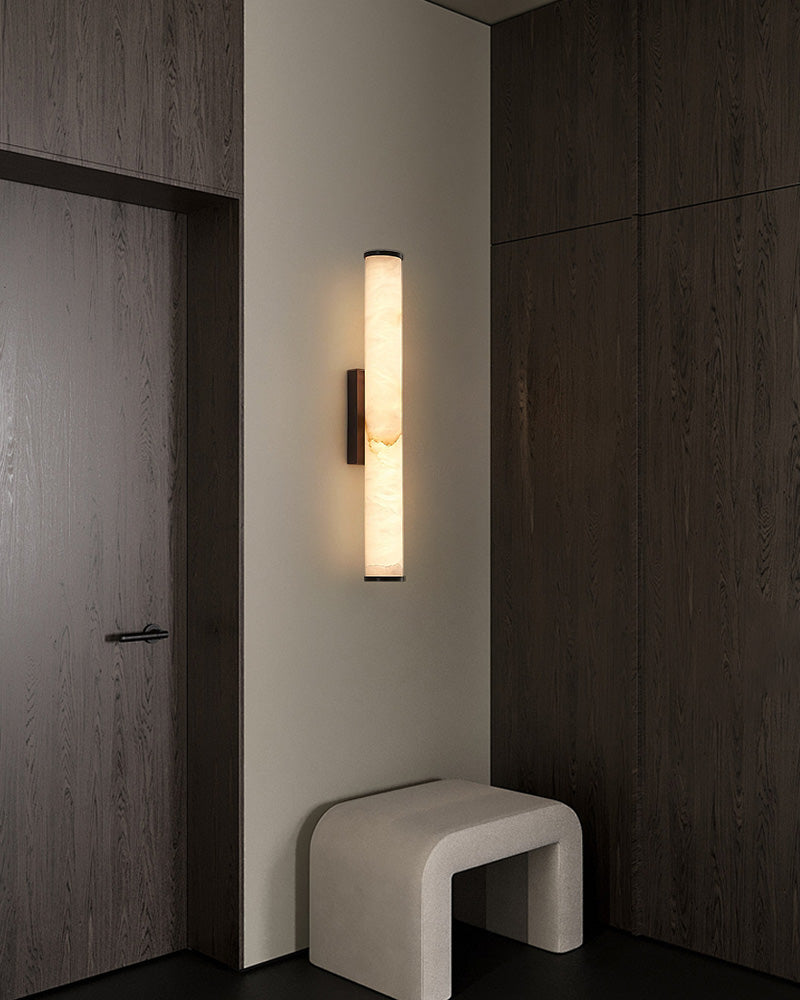 Cylindrical alabaster wall sconce lamp illuminating dark wooden interior design.