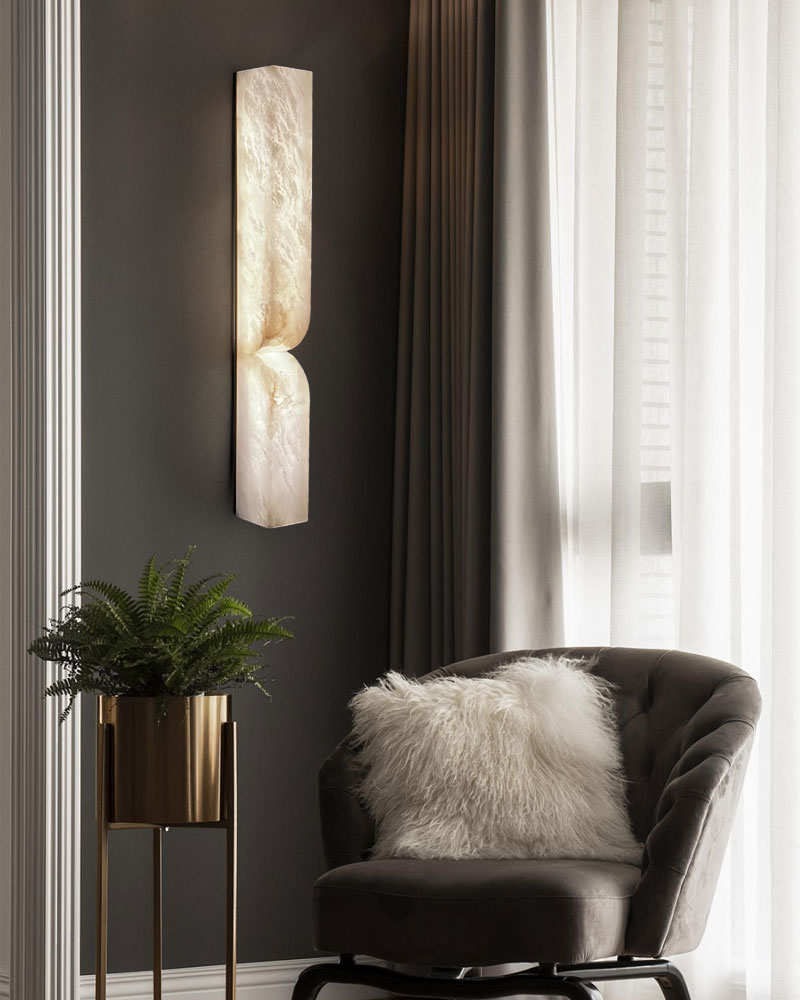 Elegant alabaster wall sconce casting warm light beside a cozy gray chair with fur cushion.