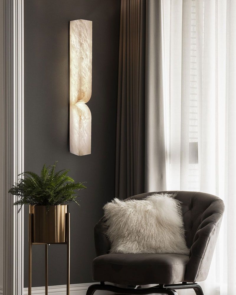 Elegant alabaster wall sconce casting warm light beside a cozy gray chair with fur cushion.