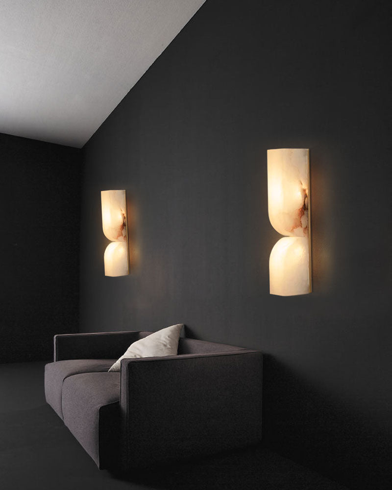 Elegant alabaster wall sconces on black wall beside modern gray sofa in minimalist setting.