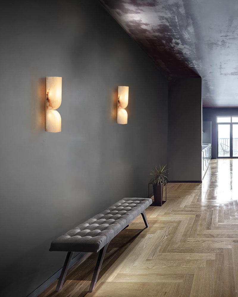 Sleek gray tufted bench with alabaster wall sconces in stylish entryway