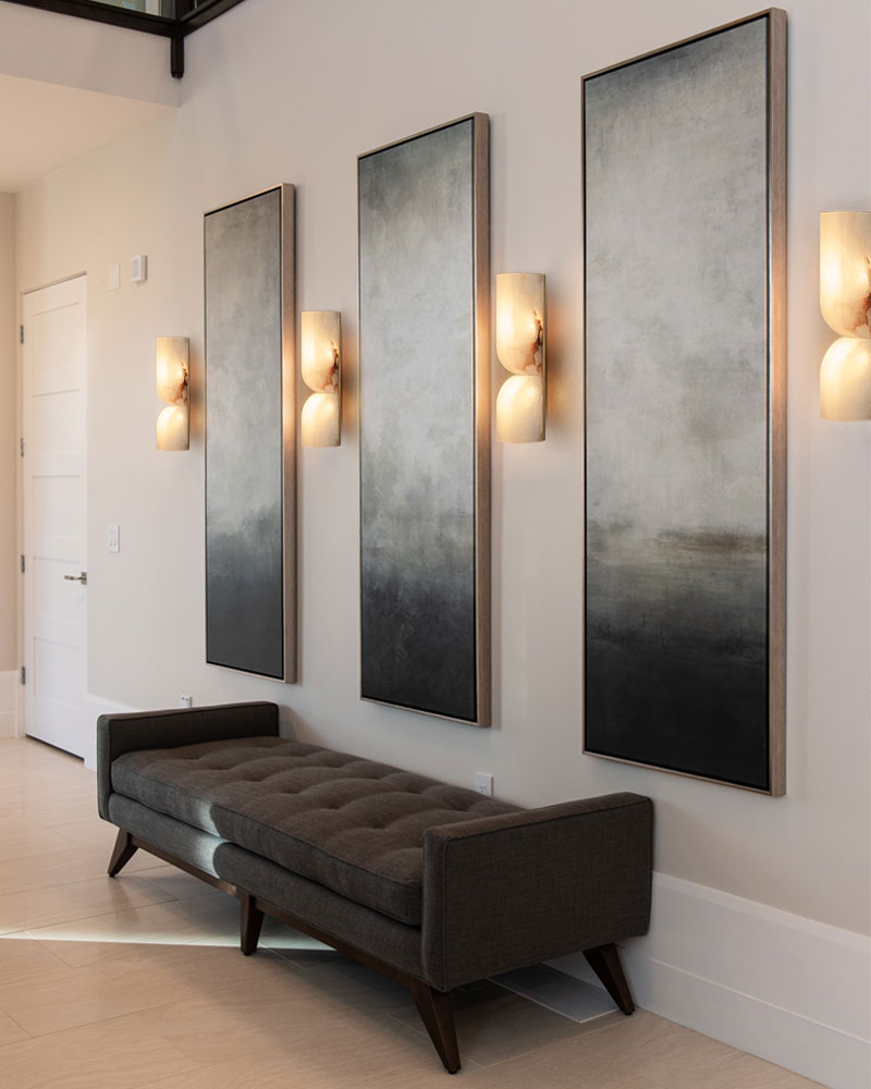 Modern entryway with gray tufted bench, abstract art, and elegant wall sconces