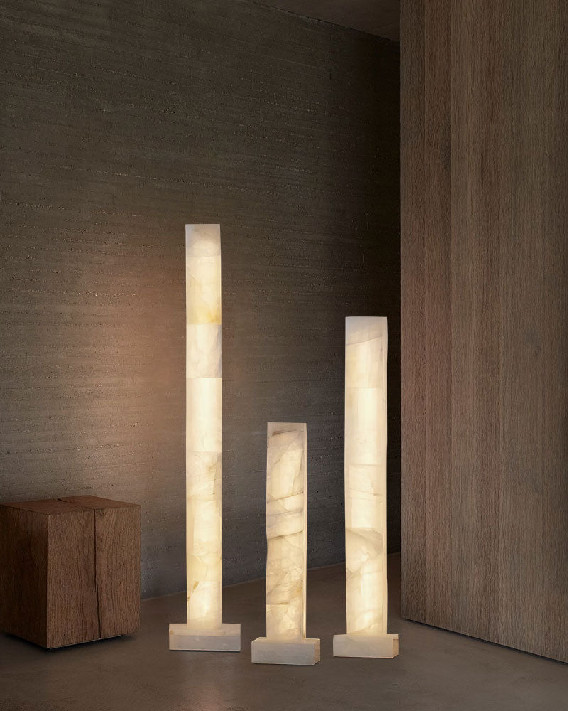 Set of three tall alabaster column floor lamps glowing softly in modern interior