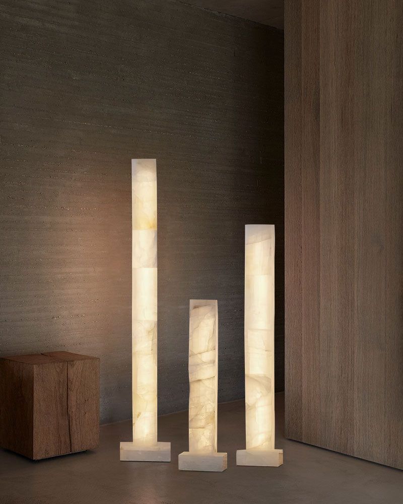 Set of three tall alabaster column floor lamps glowing softly in modern interior