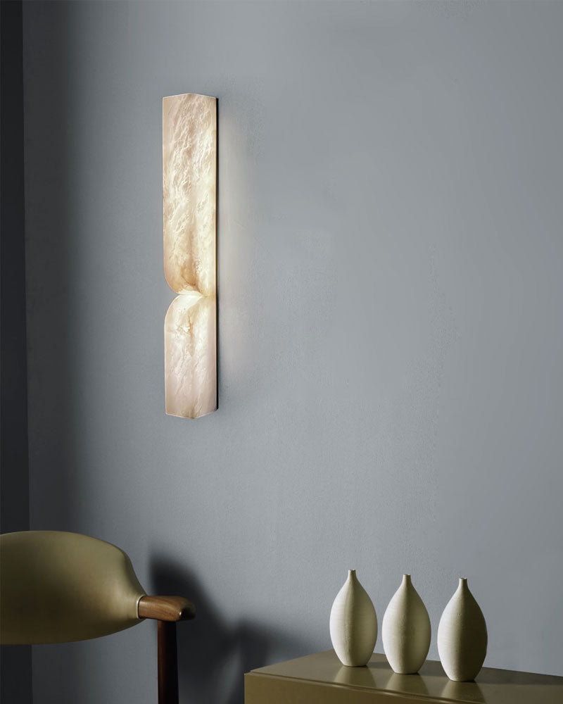 Elegant alabaster wall sconce illuminating gray wall near decorative vases and chair.